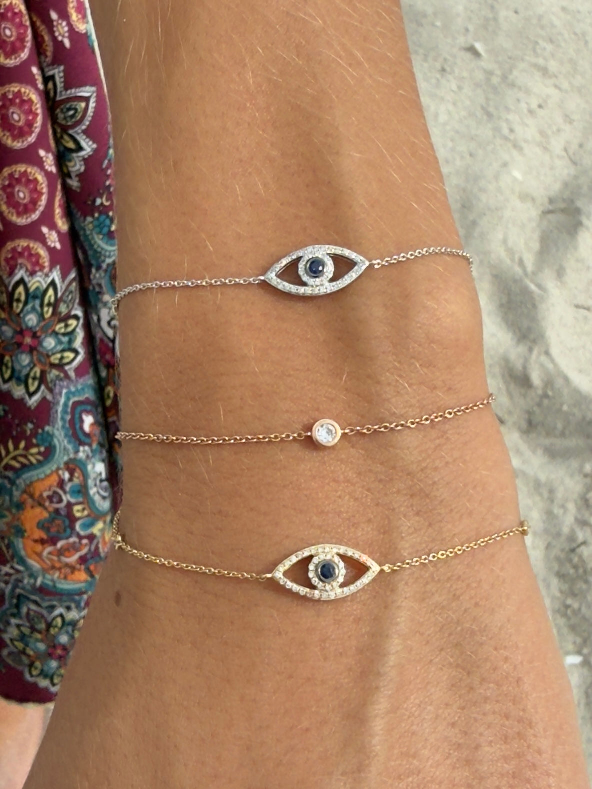 Hand with stacked bracelets including Samba No Pé bezel solitaire chain bracelet and Watchful Eye Bracelets