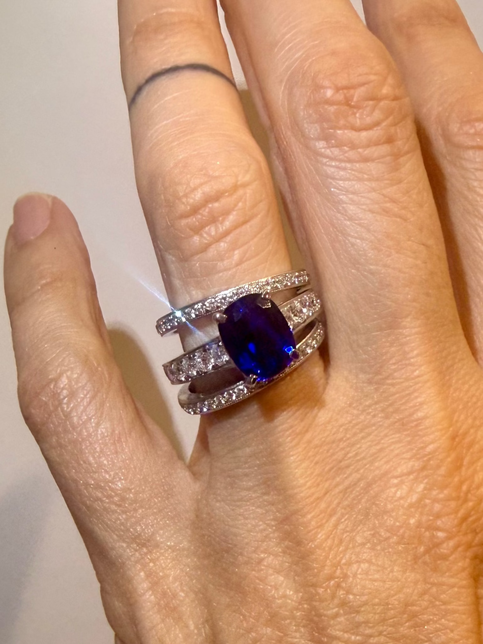 Blue Nilu ring with blue sapphire cushion-cut center stone with diamond band styled with  wedding bands on Nilu's hand—Waltz Diamonds
