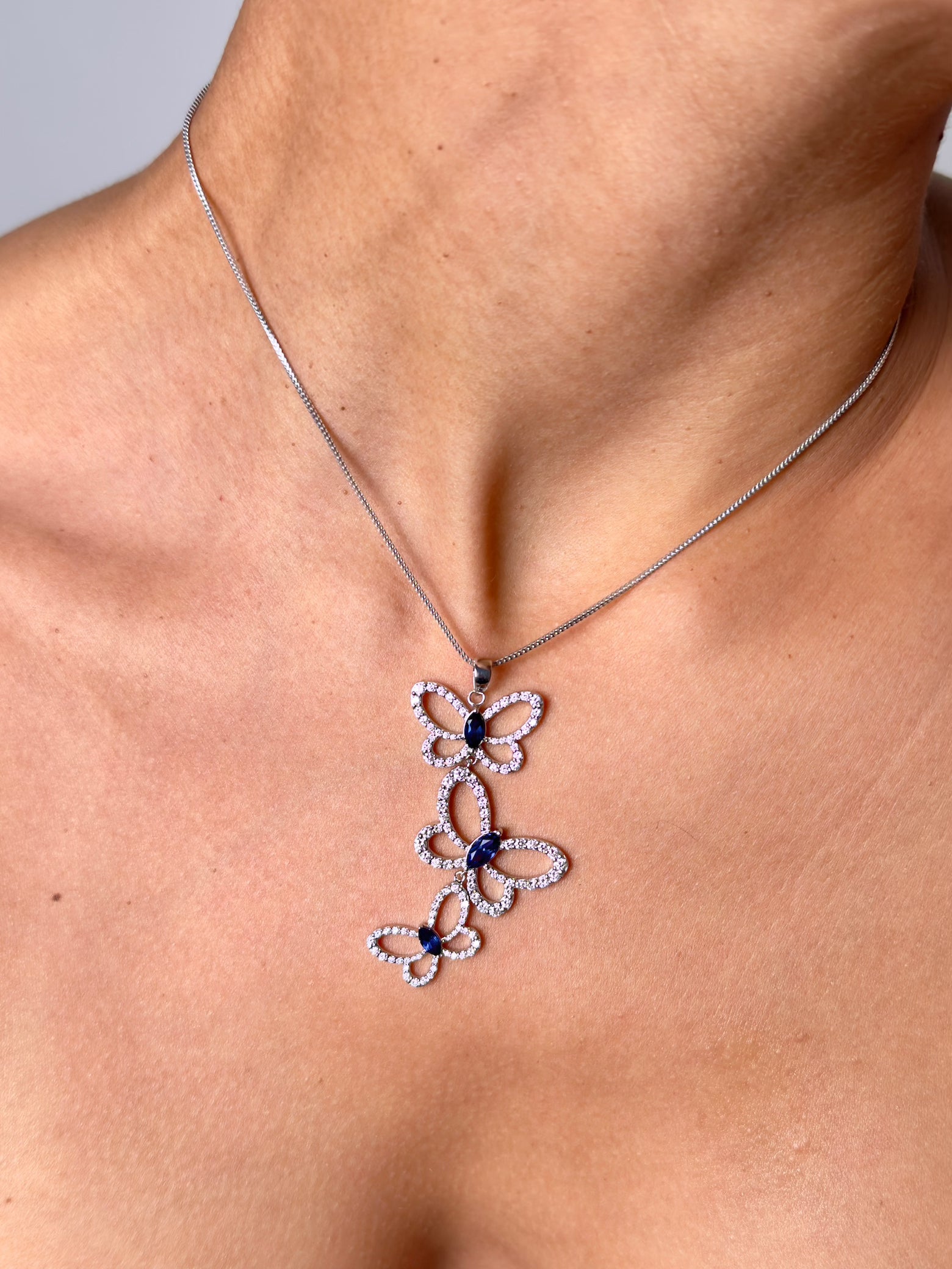 Butterfly effect pendant in white gold featuring 3 butterflies with marquise blue sapphire center stones on model — Waltz Diamonds