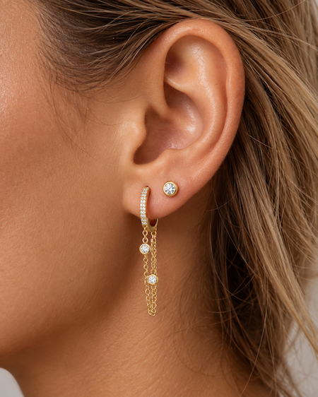 Looped in diamond chain huggies featuring a diamond pave huggie with a double looped chain with two bezel set diamonds yellow gold on ear — waltz Diamonds