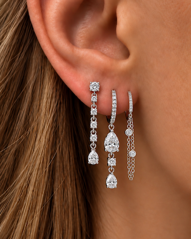 Looped in diamond chain huggies featuring a diamond pave huggie with a double looped chain with two bezel set diamonds white gold styled on ear — waltz Diamonds