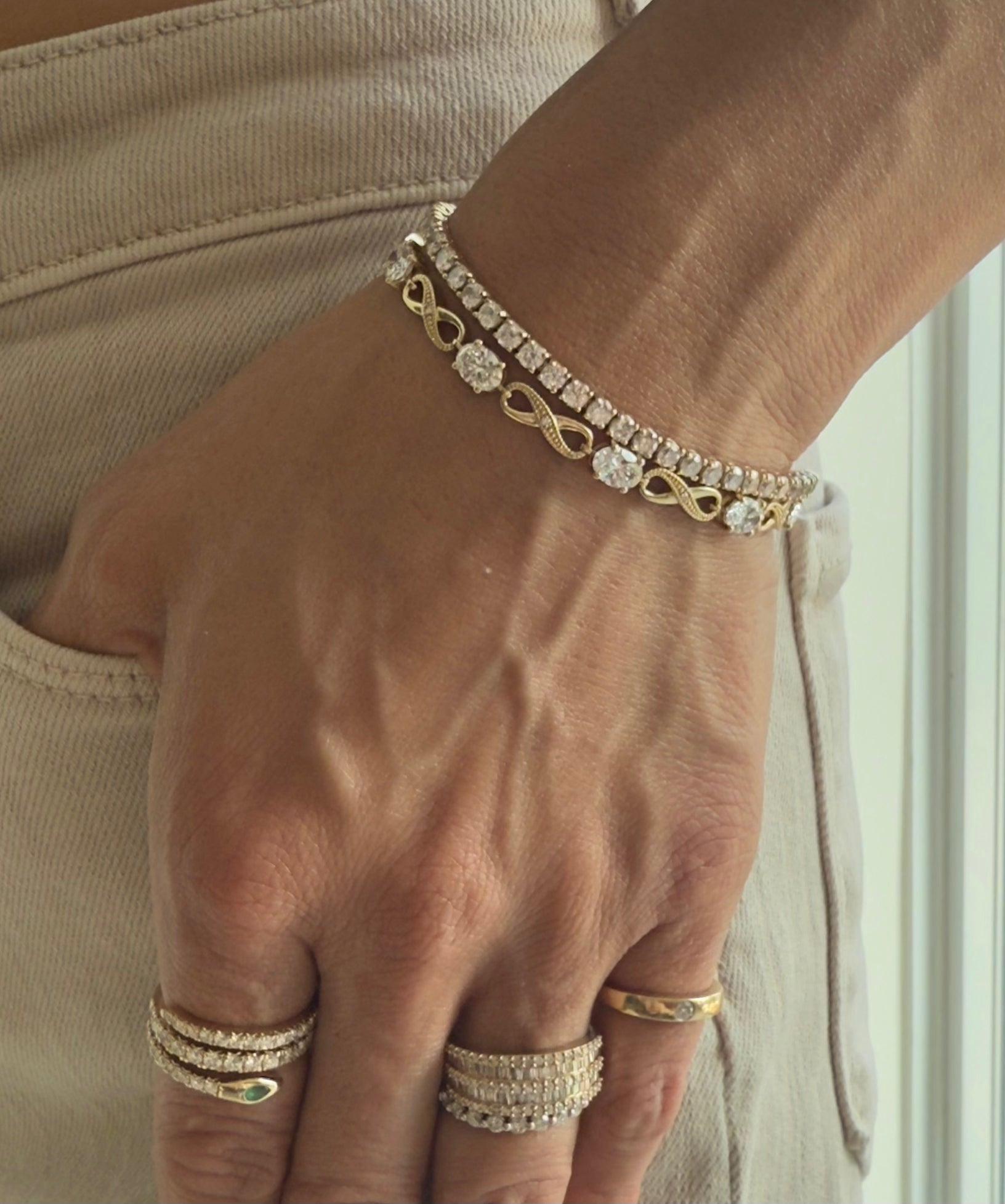 Hand wearing the abundance bracelet in yellow gold, styled with rings and bracelets from the same brand