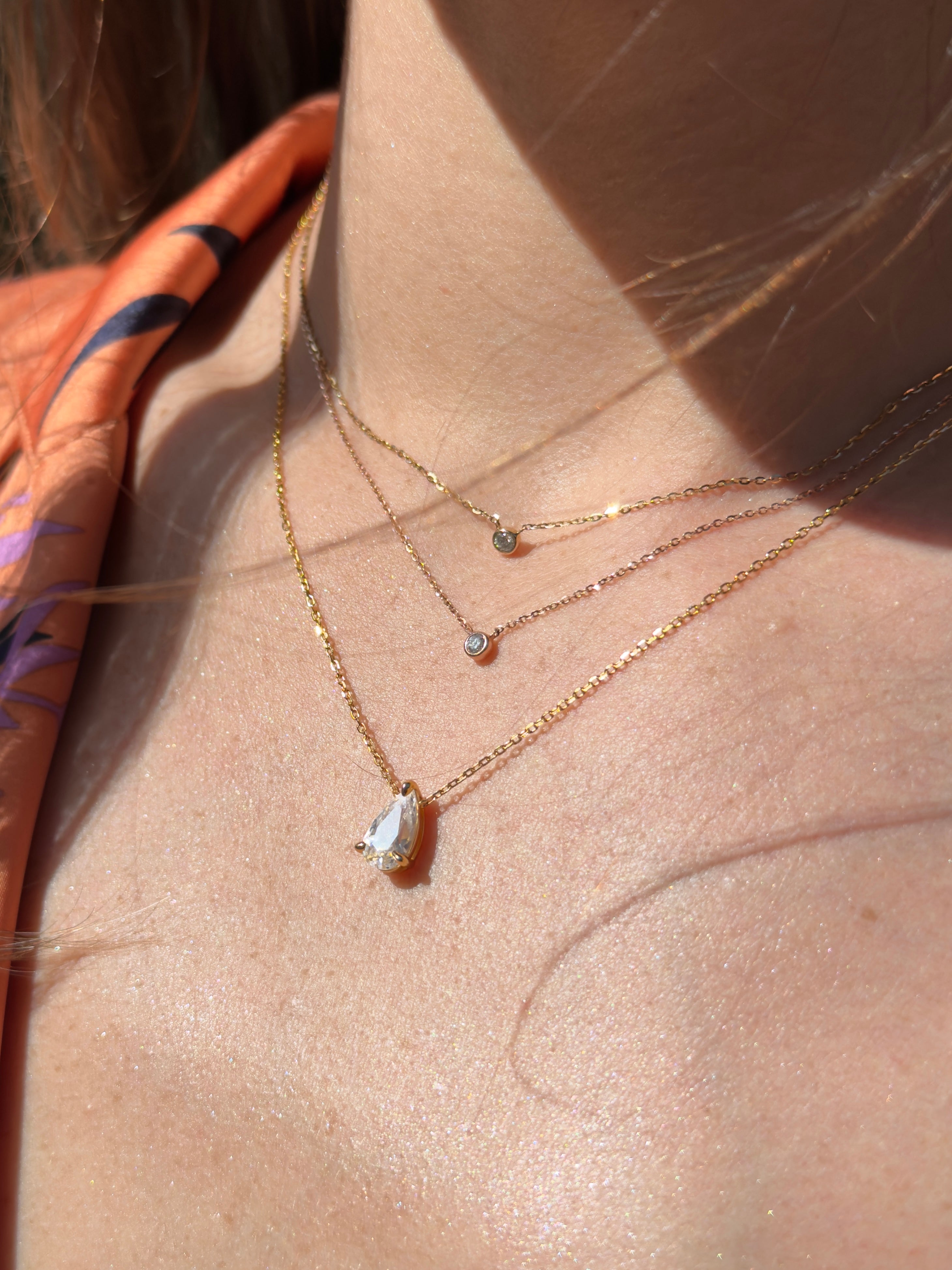Model wearing layered Baby Bezel Diamond Necklace and For the Planet Pear Solitaire pear-cut diamond necklace for stacked look